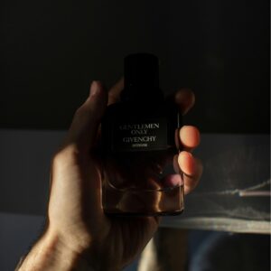 A man's hand holds a Givenchy perfume bottle with dramatic lighting.